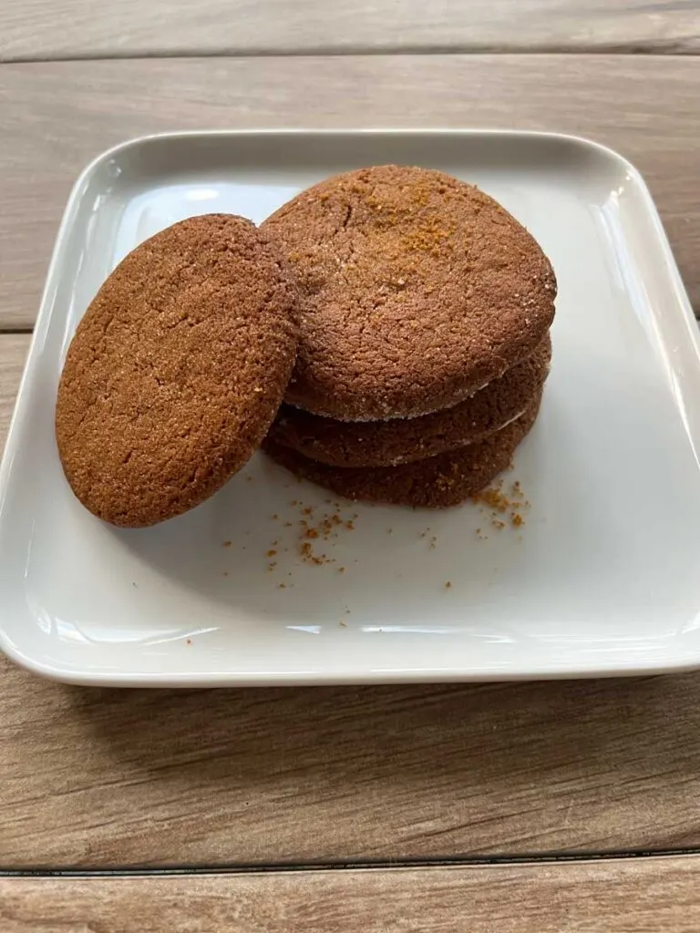 Stack of cookies with 1 cookie leaned against the stack on a white square plate on top of a wood surface