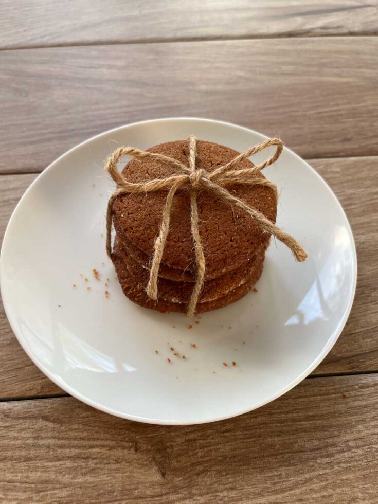 stack of molasses cookies with twine tied around them, sitting on a round white place onto of a wood surface