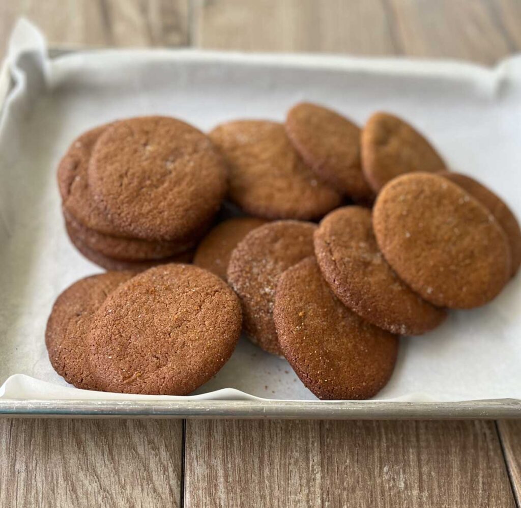 Molasses cookies on a small tray with white parchment paper under the cookies. Tray is on a wood surface