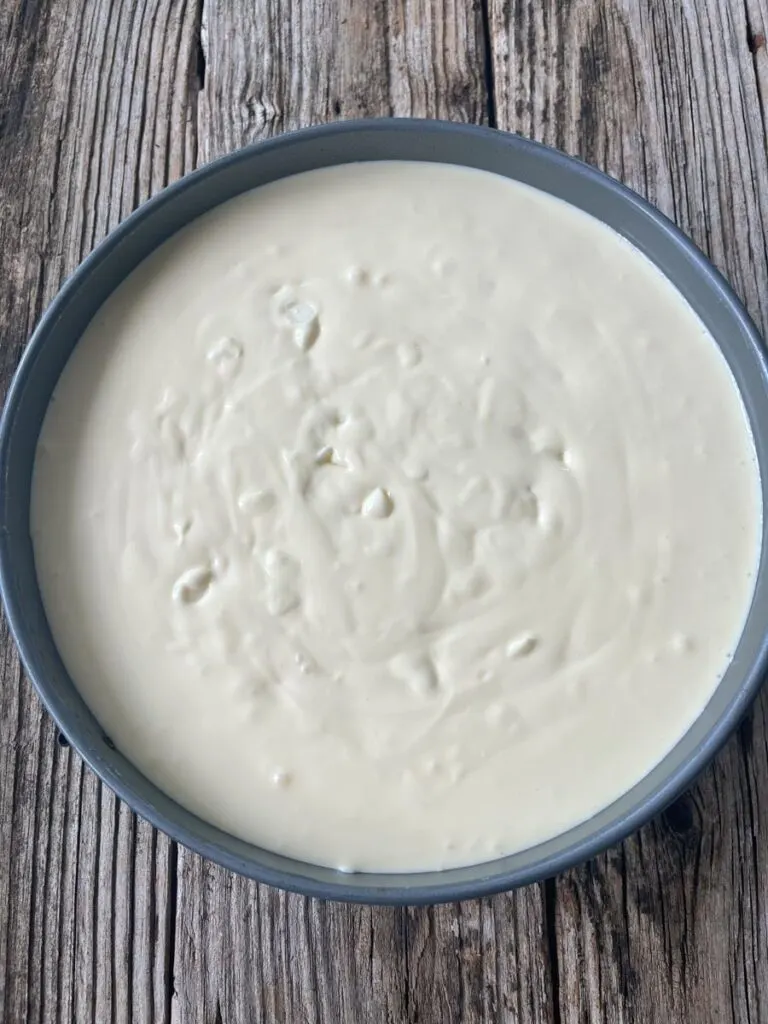 White chocolate chip cheesecake batter in a 9 inch springform pan sitting on a wood surface