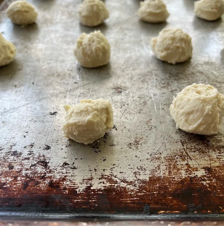 Rows of uncooked cookie dough in the shape of small balls on a cookie baking pan.