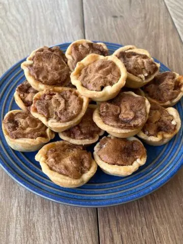 Blue plate stacked with mini pecan tarts on a wood surface
