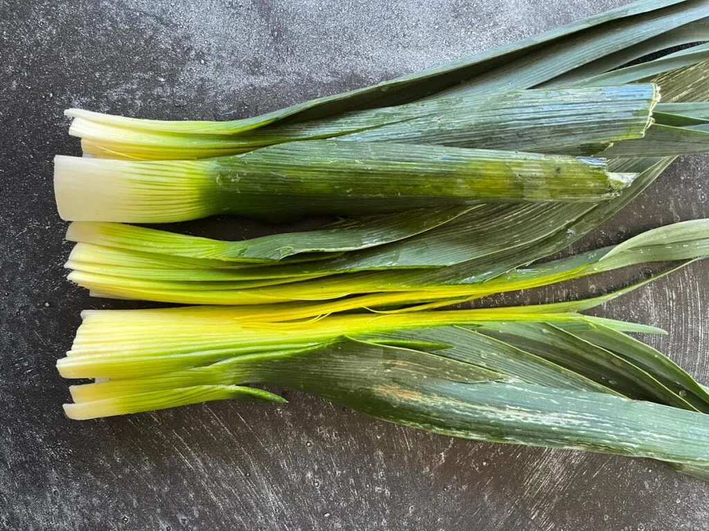 Two leeks cut in half lengthwise on a gray surface.