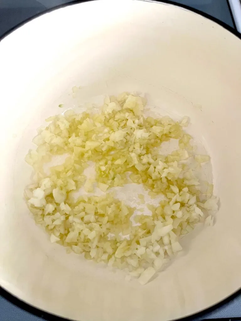 Chopped onion in olive oil cooking in a large white ceramic pot