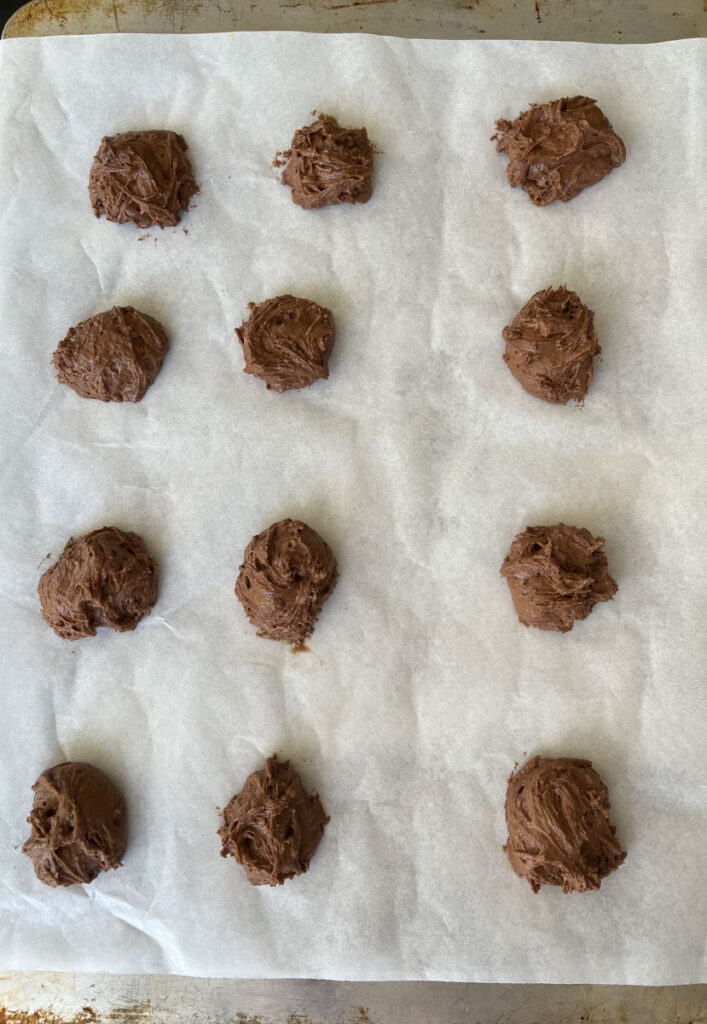 Twelve chocolate cookie dough balls on a parchment paper lined cookie sheet.