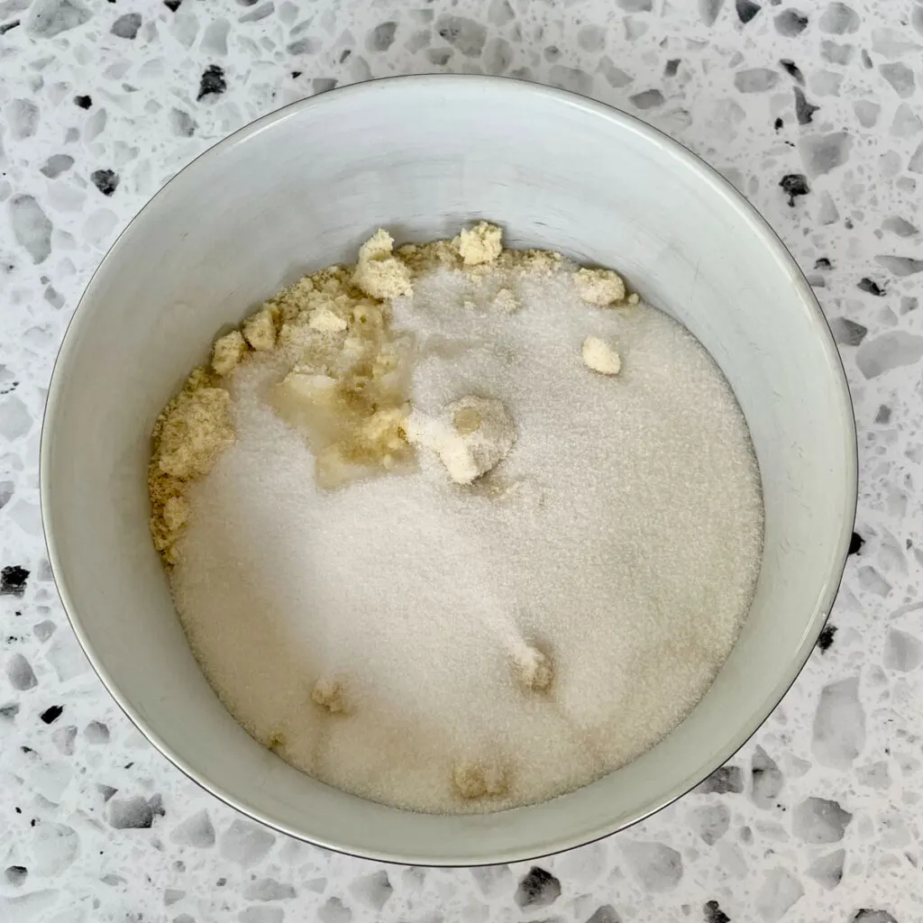White large mixing bowl with almond flour, sugar and salt in it. Bowl is on a white and black terrazzo surface.