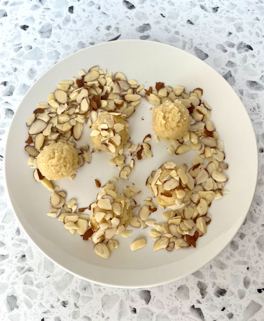White round plate with four round cookie dough balls and sliced almonds on it. The plate is on a white and black terrazzo surface.