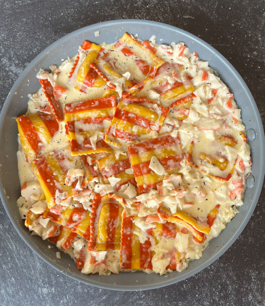 Gray skillet with red and yellow stripped pasta squares, pink cream sauce in it. Pan is on a dark gray surface.