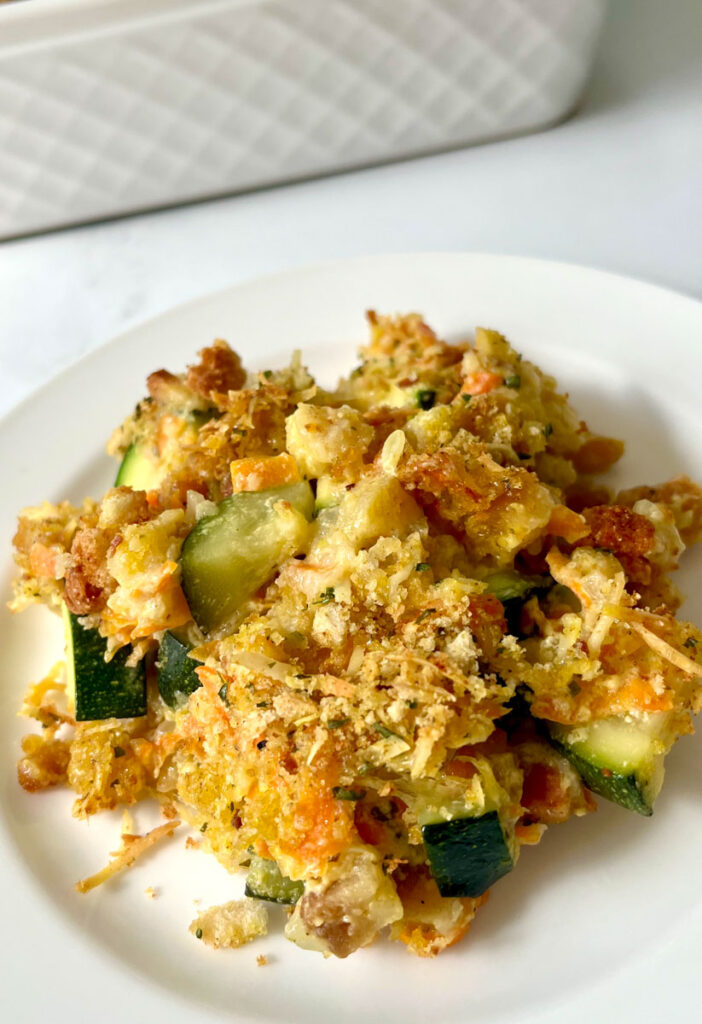 Small white plate with a scoop of baked zucchini with carrots, onions, soup, sour cream, and seasonings. Plate is on a white marbled surface.