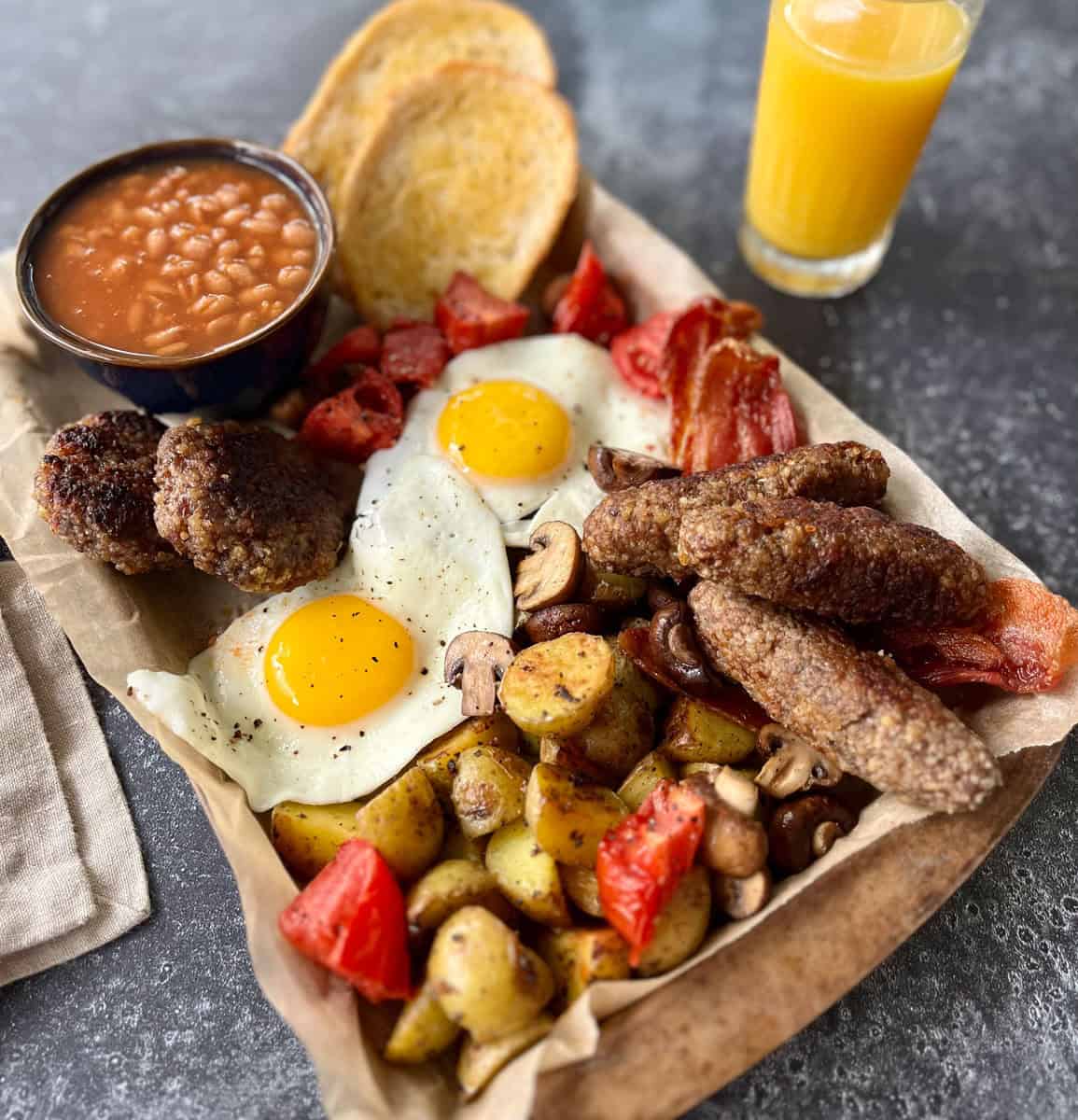 Tray with a variety of breakfast food items and a glass of orange juice on a gray counter