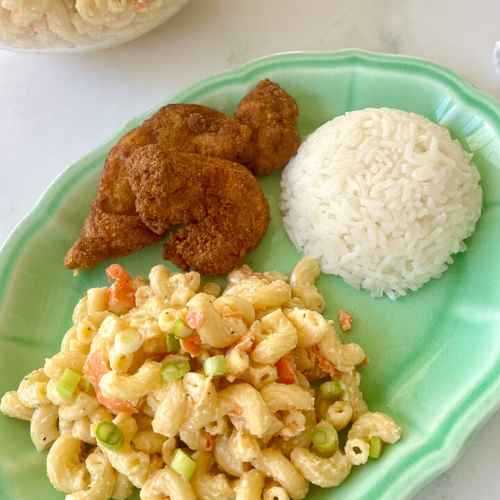 There is a green rectangular plate. On the plate there is a scoop of cooked elbow noodles, chopped carrots, grated onions, and a creamy white sauce mixed together. There is also a scoop of white rice and two pieces of fried boneless chicken on the plate.