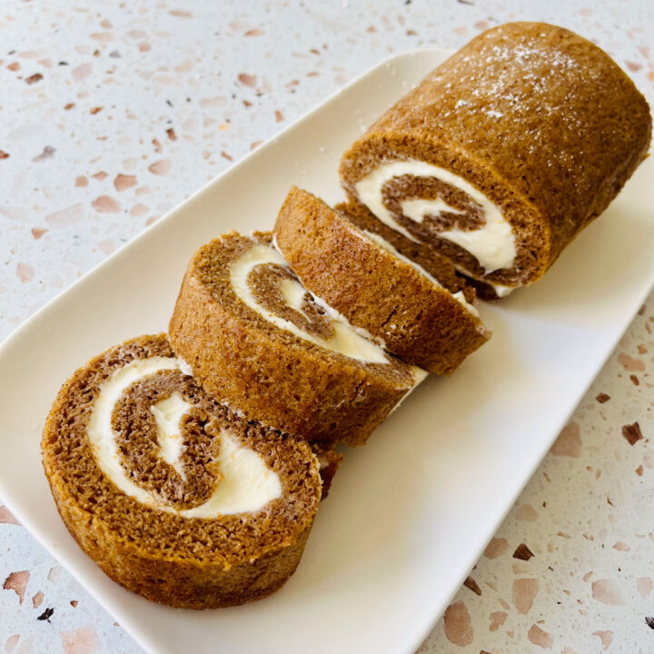 There is a small white rectangular platter with slices of a pumpkin roll on it. Platter is on an orange terrazzo surface.
