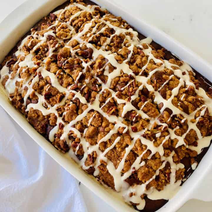 There is a white rectangular baking dish with a pumpkin coffee cake in it. There is a white cloth napkin laying beside the dish. Items are on a white surface.