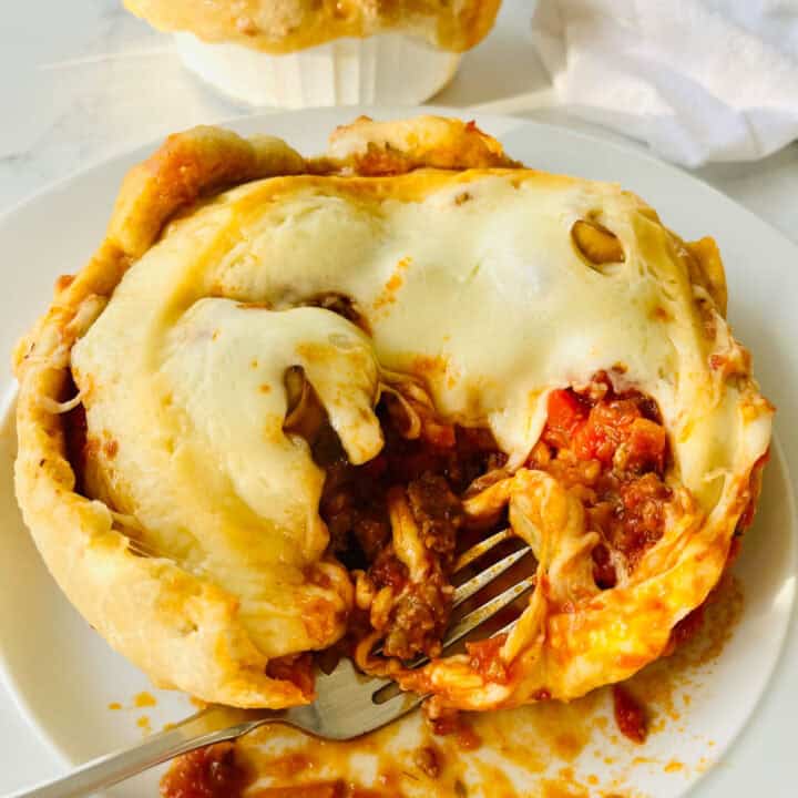 There is a white plate with part of a flipped over, out of the dish pizza on it. There is a fork resting on the plate. In the background there is a white bowl with a thick baked crust on top of it. Items are on a white surface.