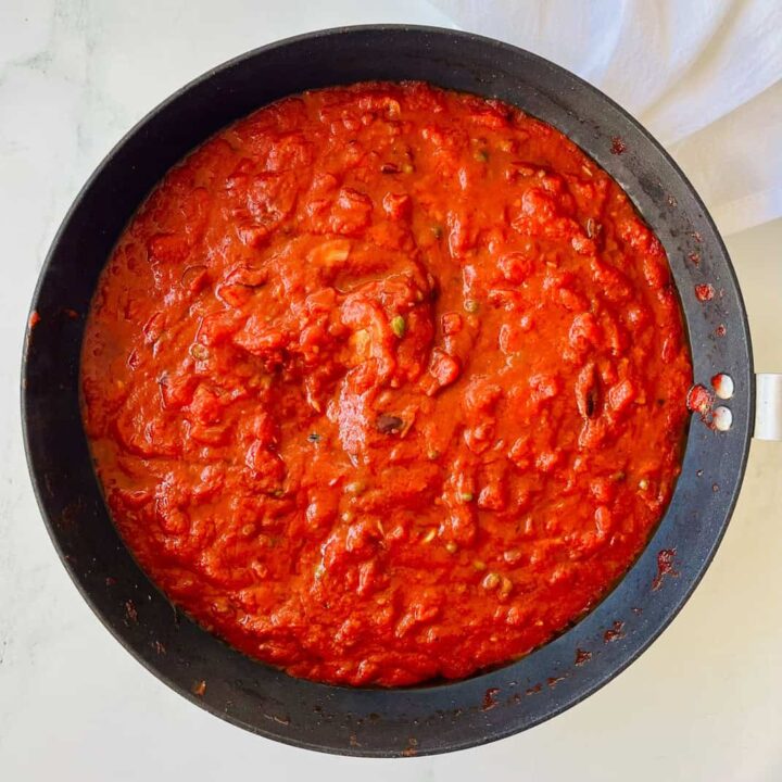Large dark gray skillet with vegan puttanesca sauce in it. Pan is on a white surface.