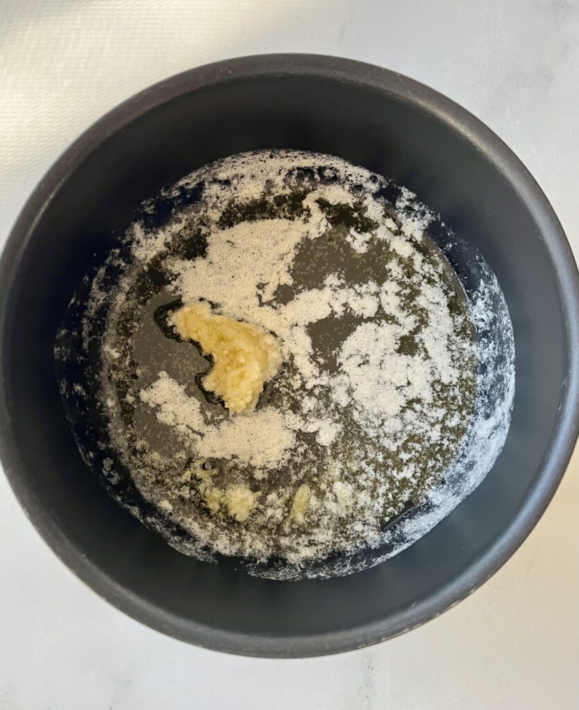 Dark saucepan with melted butter and minced garlic. Pan is on a white surface.