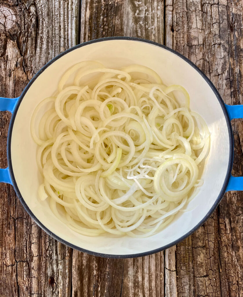 Large pot with thinly sliced onions in it. Pot is on a wood surface.