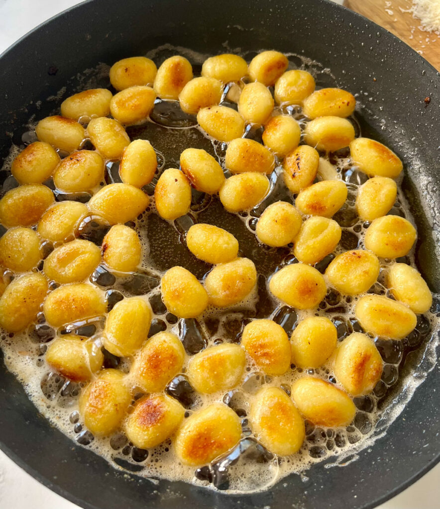 There is a large skillet with cooked gnocchi in melted butter.