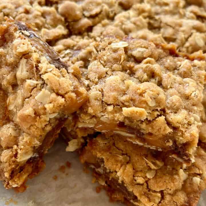 There is a pile of oatmeal layered bar cookies on a piece of white paper.