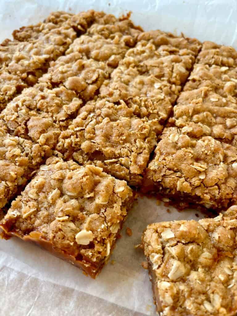 There are square oatmeal cookie bars in a single layer on white paper.