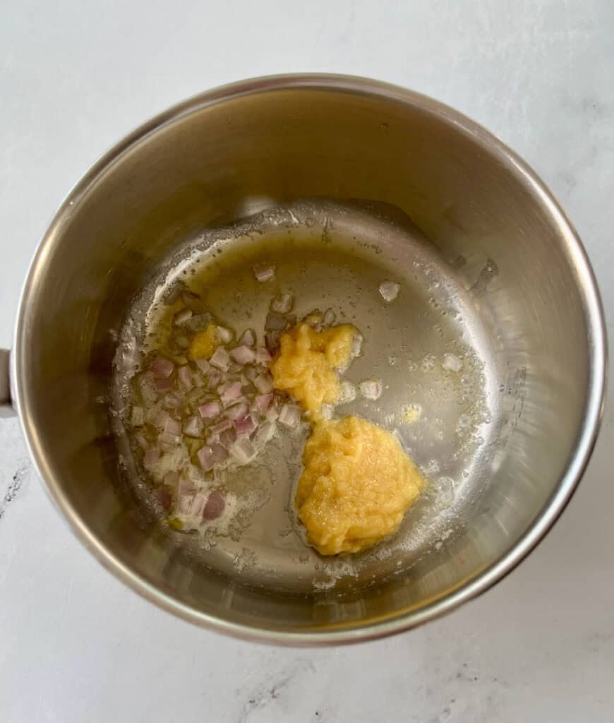 There is a saucepan with ginger paste, diced shallots and a little butter cooking. Pan is on a white surface.