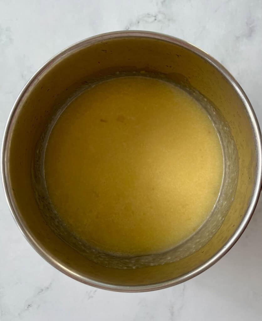 There is a saucepan with a yellow sauce in it. Pan is on a white surface.