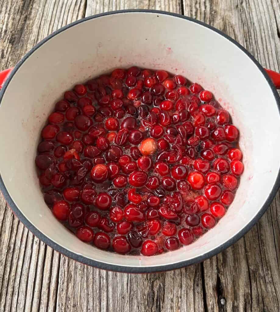 A pot filled with cranberries sitting on a wooden table.