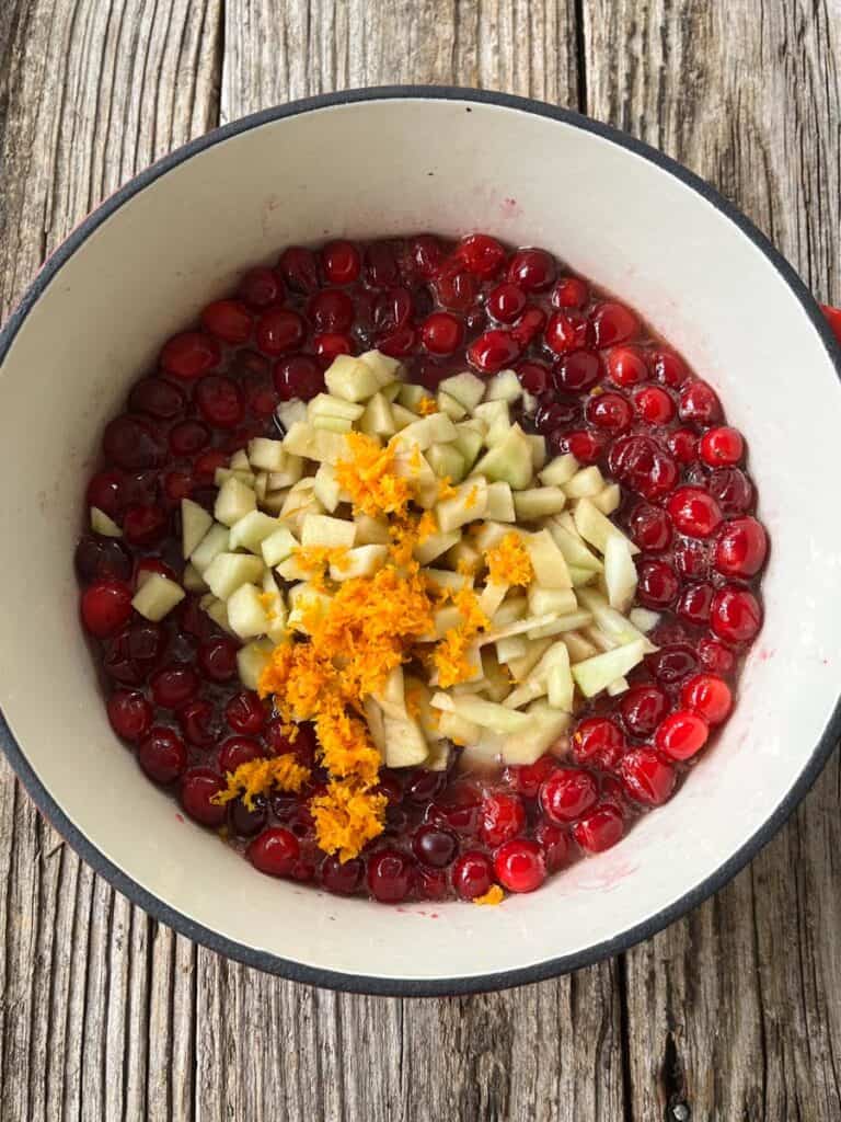 A pot filled with cranberries, apples, and orange slices.