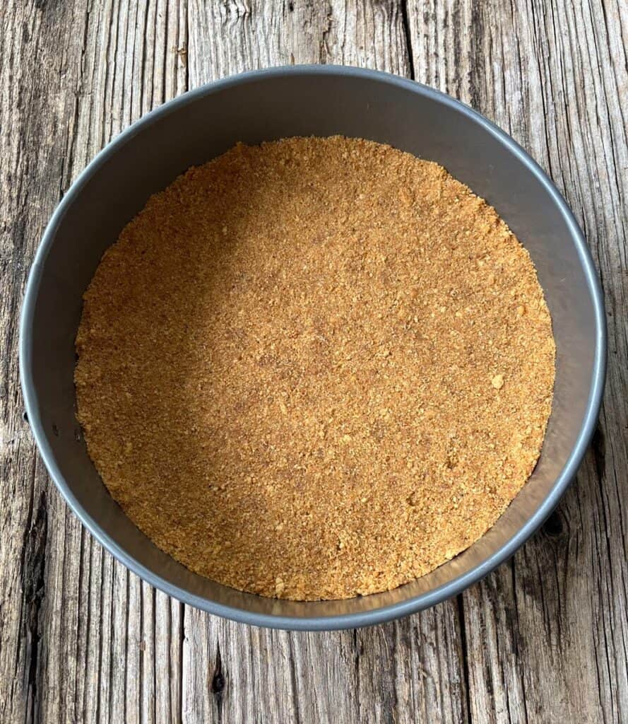 A graham cracker crust in a pan on a wooden table.