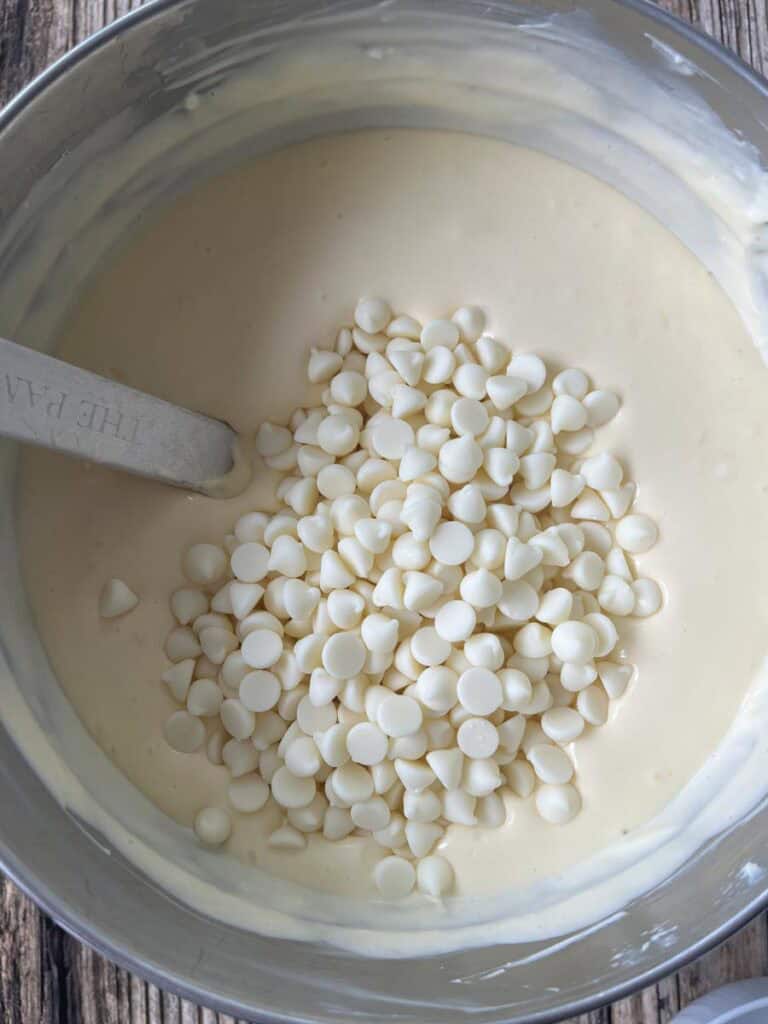 A bowl filled with a cream cheese mixture and white chocolate chips and a spatula.