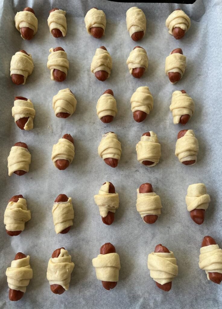 Unbaked hot dogs wrapped in dough on a baking sheet.
