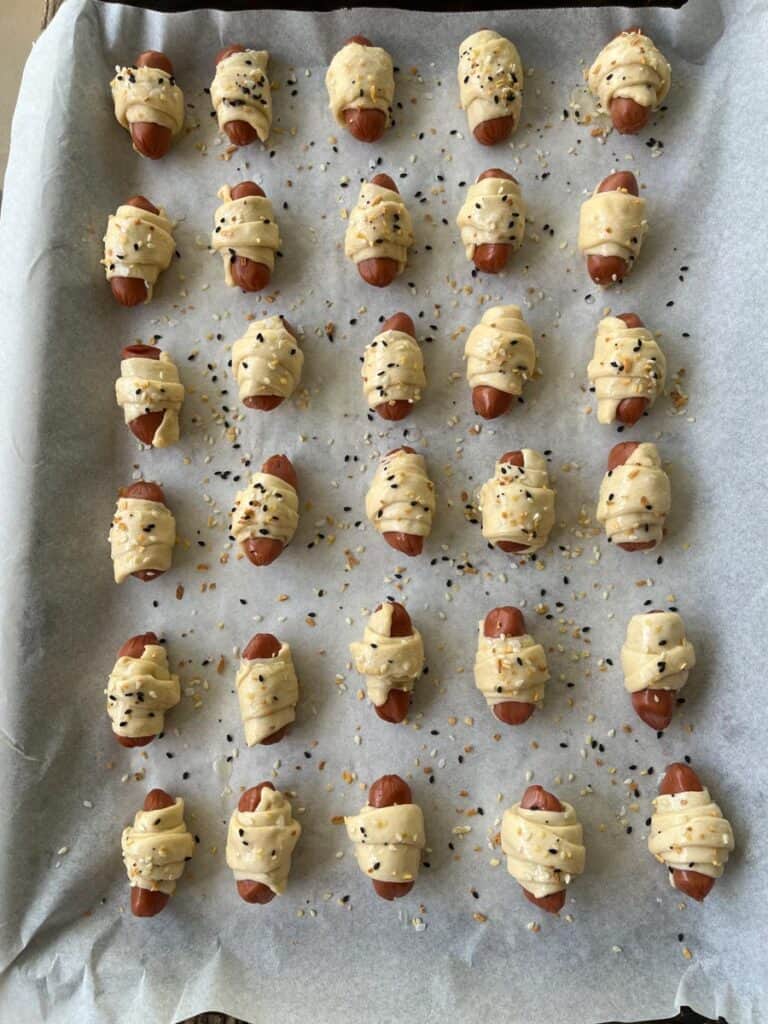 A baking sheet with a bunch of hot dogs wrapped in dough.