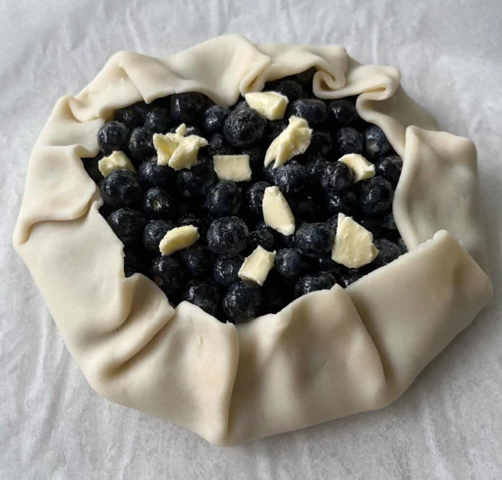 A pie crust with blueberries and butter cubes.