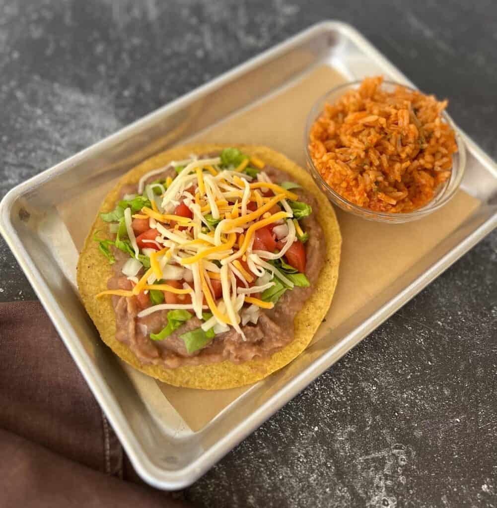 A tostada on a metal tray with a side dish.
