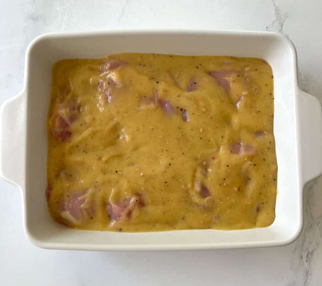 A white dish with uncooked chicken and cheese in it.