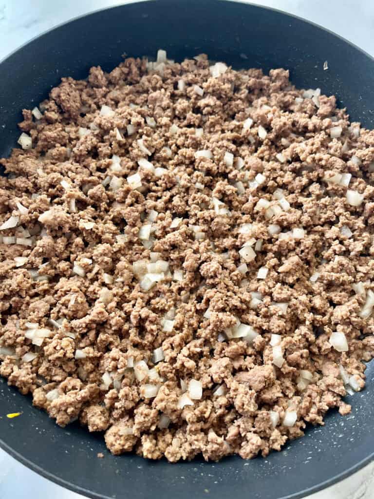 Large black skillet with a cooked ground beef mixture and chopped onion in it.