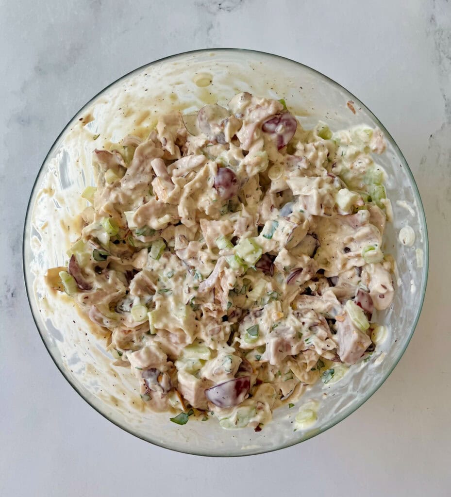 There is a large clear glass bowl with chicken salad in it. Bowl is on a white surface.
