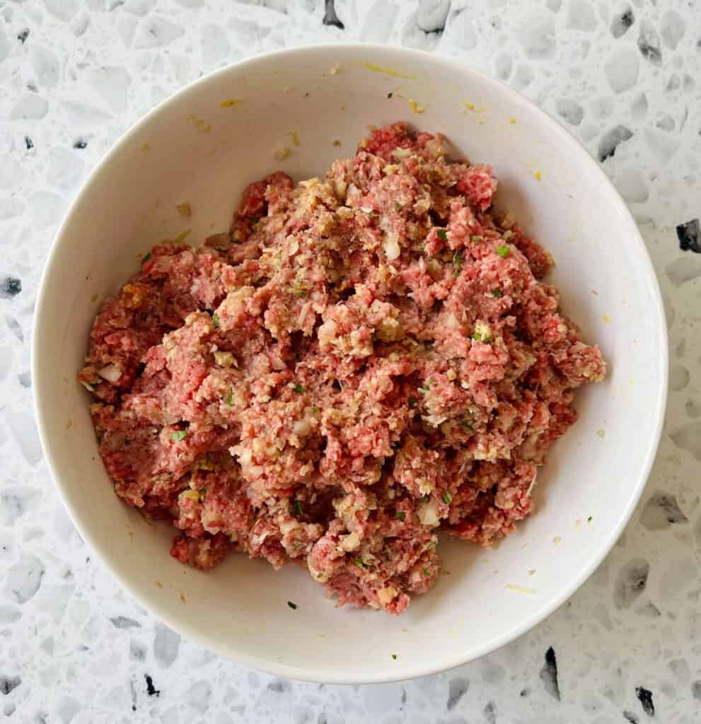 There is a large white bowl with a ground beef mixture in it. Bowl is on a black and white terrazzo surface.