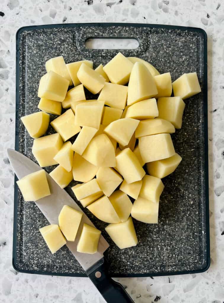 A cutting board with cubed potatoes and a knife.