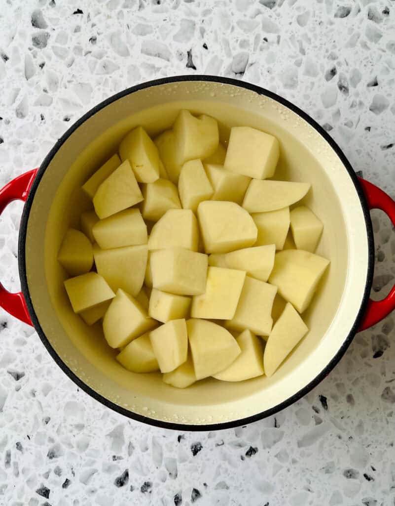There is a large pot with chunks of potato and water in it.