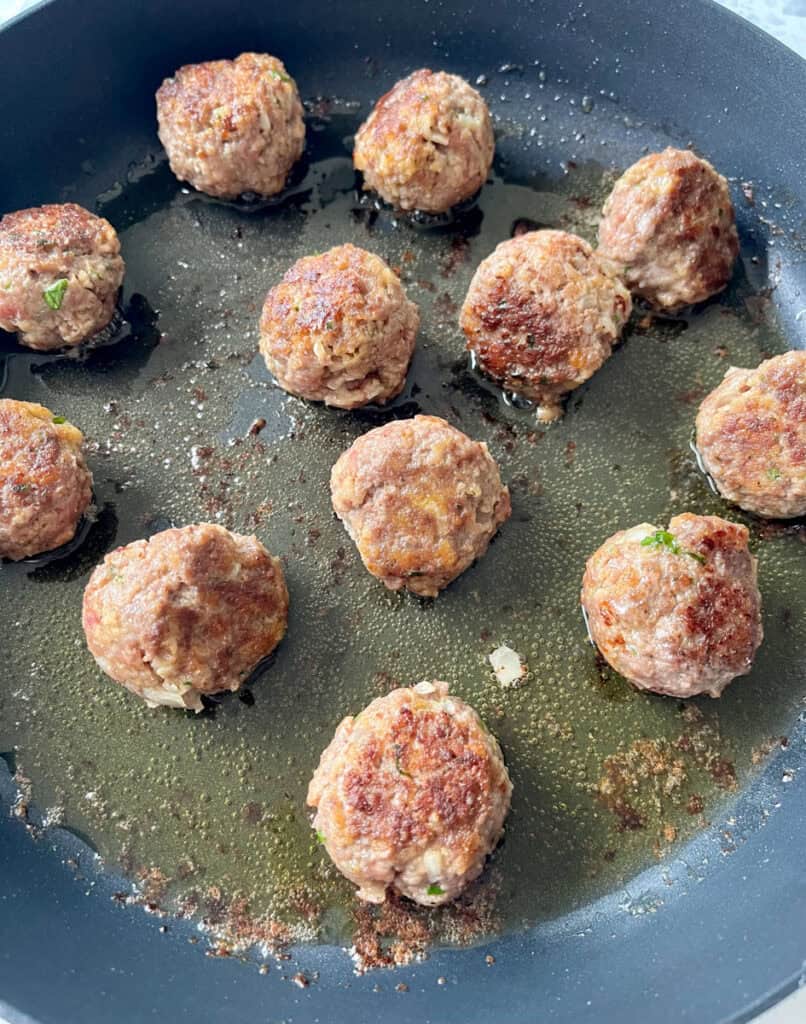 There is a large dark skillet with meatballs cooking.