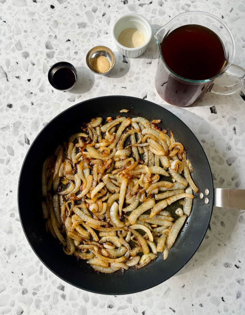 A pan filled with cooked onions. There is a cup of broth.