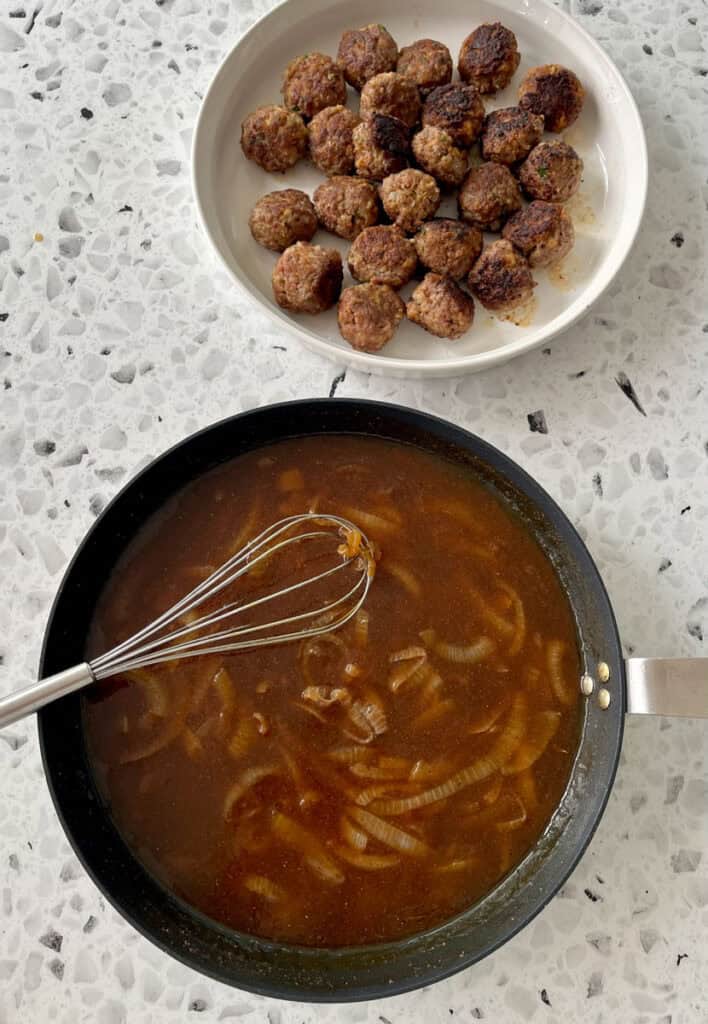 A pan with sauce next to a bowl of meatballs.