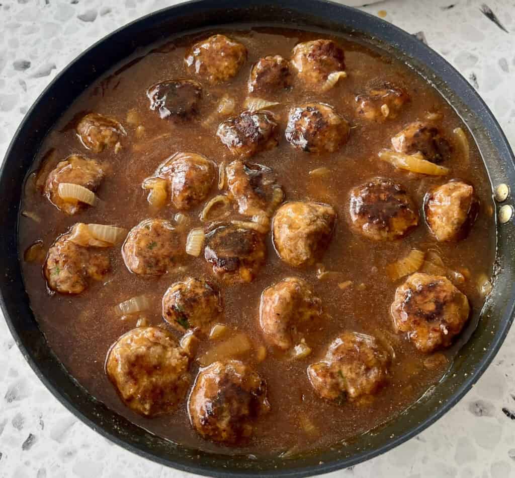 A pan filled with meatballs, sauce, and onions.