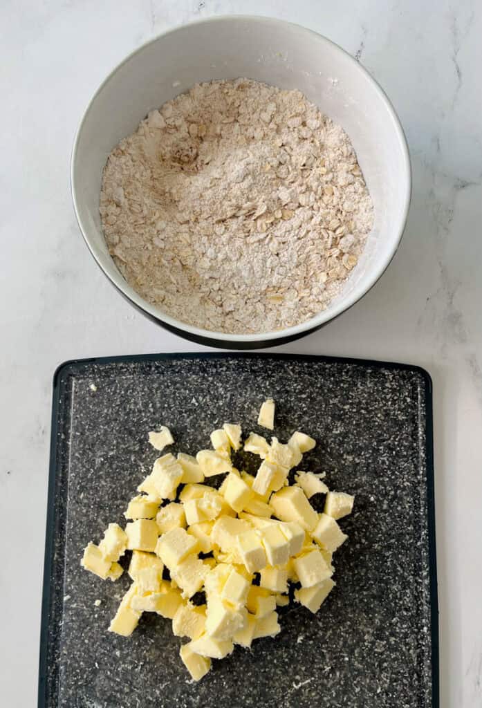 A bowl of flour and a cutting board with chopped up butter.