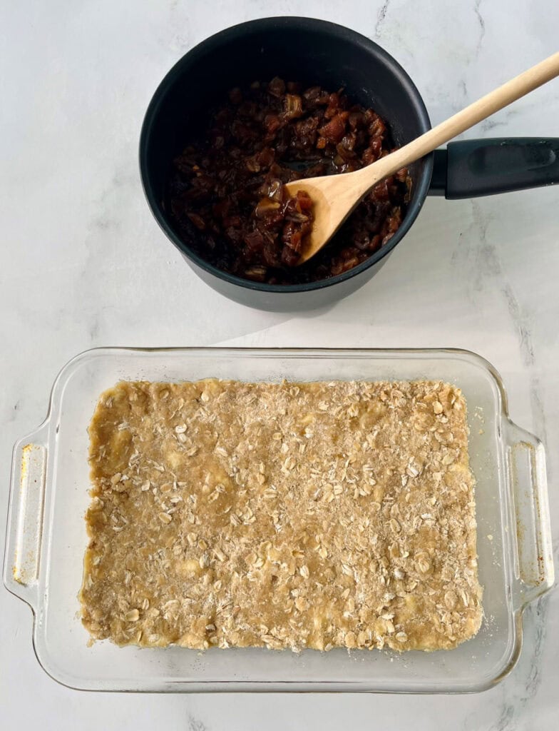 A pan filled with oatmeal crumble and a saucepan with cut up dates and wooden spoon in it.