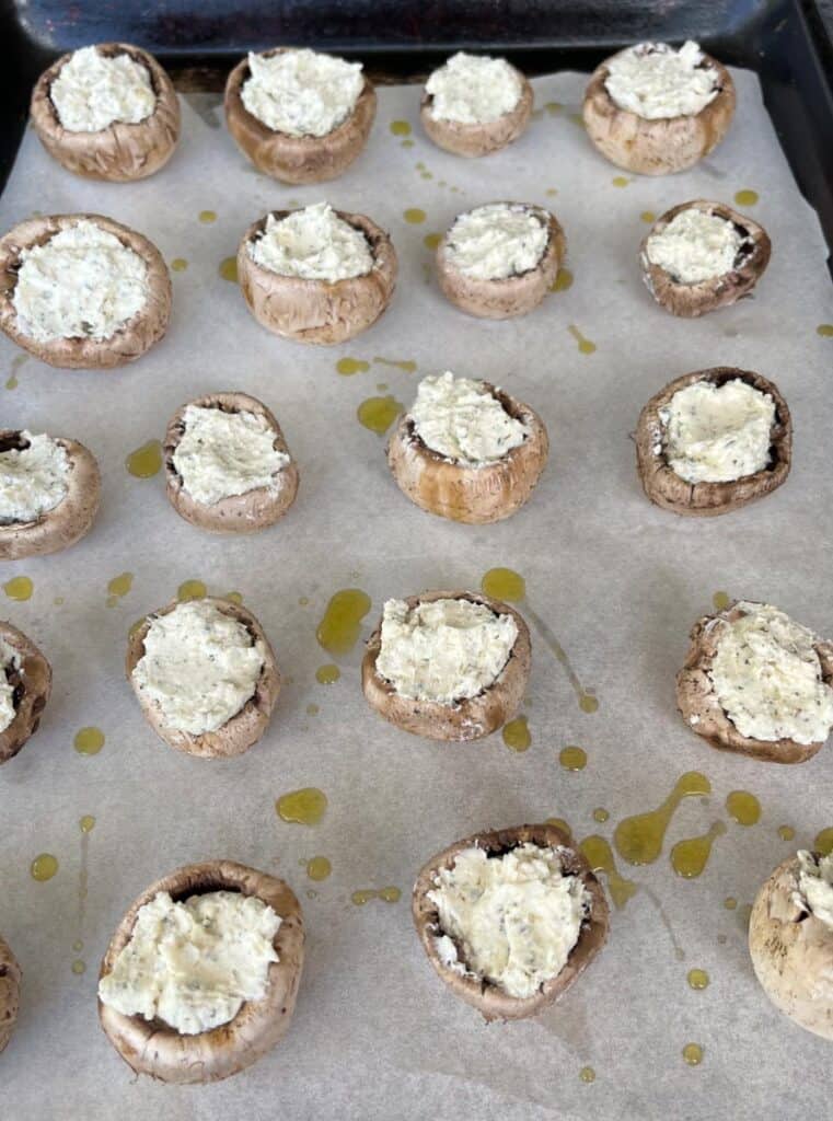 Unbaked stuffed mushrooms with cream cheese on a baking sheet.