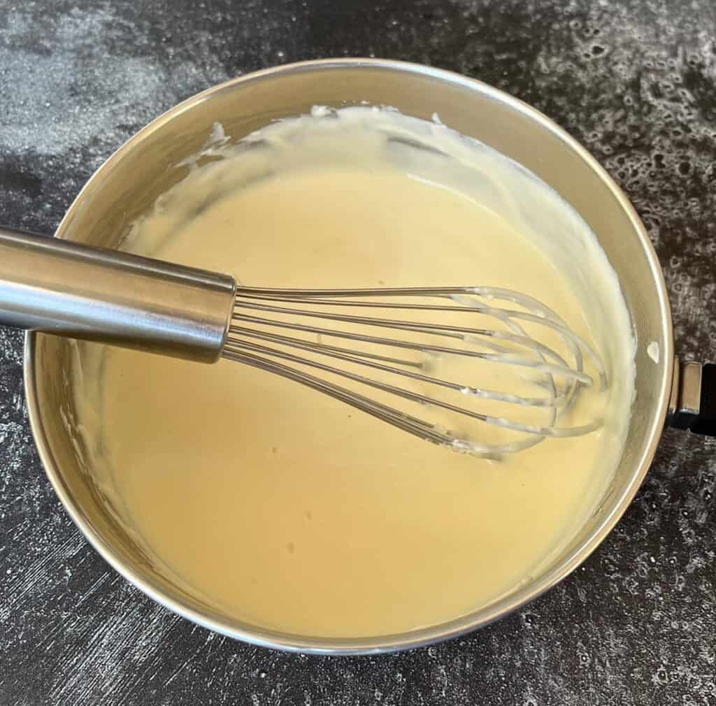 A whisk in a pan with cheese sauce.