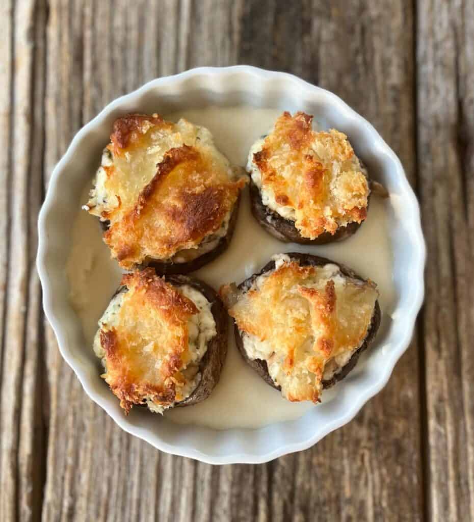 A round shallow dish with four stuffed mushrooms on a bed of cheese sauce.