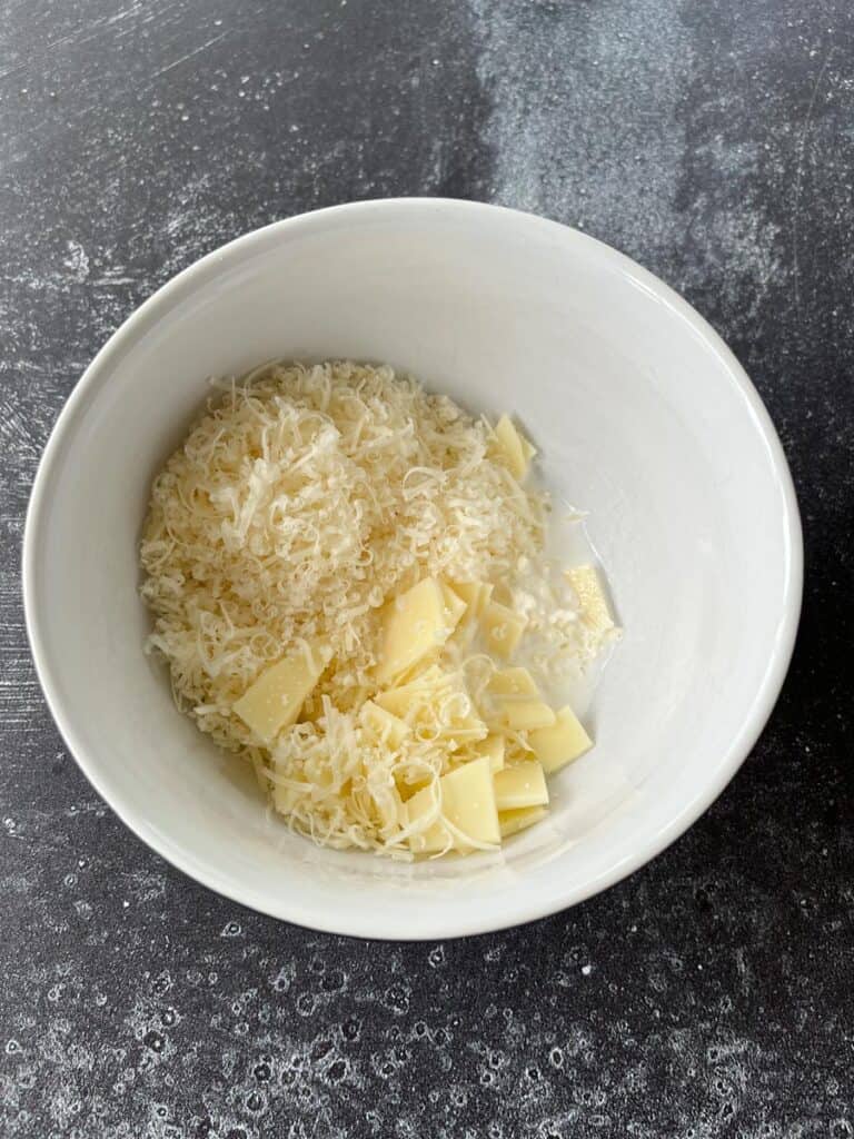 A white bowl filled with shredded and sliced cheese.